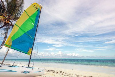 Ein farbenfrohes Segelboot steht am Strand, umgeben von Palmen und dem klaren blauen Wasser des Ozeans.