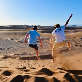 Kinder springen und haben Spaß auf den weiten Sanddünen der Sahara – Marokko Familienreise