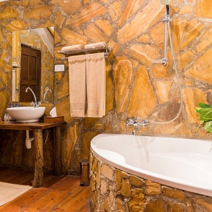 Ein rustikales Badezimmer mit Steinwänden, einer freistehenden Badewanne und einem Holzwaschtisch, der eine entspannende Atmosphäre schafft.