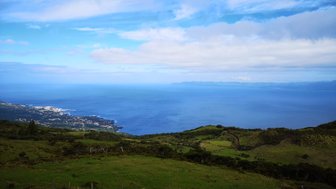 Ein atemberaubender Blick auf das blaue Meer, umgeben von sanften Hügeln und üppigem Grün unter einem klaren Himmel.