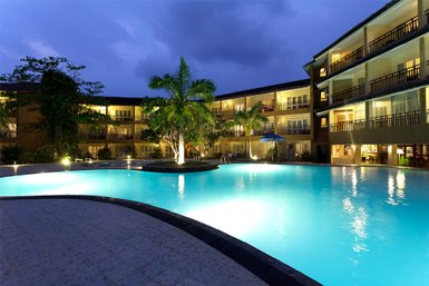 Ein beleuchteter Pool umgeben von Palmen und einem Hotel, das in der Dämmerung eine entspannende Atmosphäre schafft.