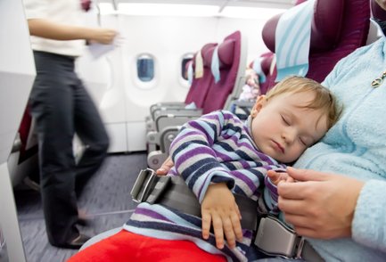 Eine ruhige Flugzeugszene mit einem schlafenden Kleinkind, das auf dem Schoß einer Person liegt, während das Personal vorbeigeht.
