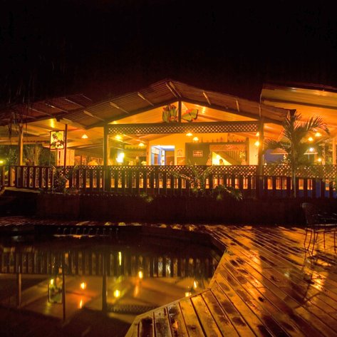 Ein einladendes Restaurant mit warmem Licht, umgeben von tropischen Pflanzen und einem ruhigen Pool im Vordergrund.