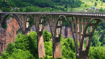 Eine beeindruckende Brücke mit eleganten Bögen, die über eine grüne Schlucht führt, umgeben von üppiger Vegetation.