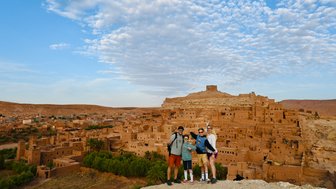 Familie lächelt für ein Foto vor den traditionellen Lehmbauten von Aït Ben Haddou – Marokko Reise mit Kindern