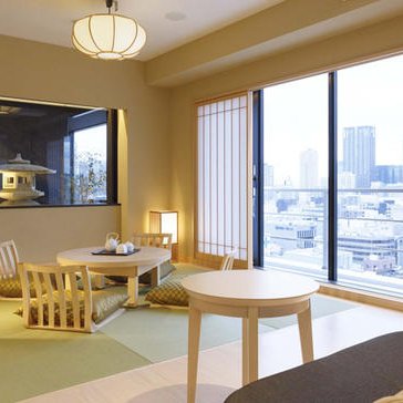 Ein stilvolles Hotelzimmer in Osaka mit tatami-Matten, einem niedrigen Tisch und einem Blick auf die Stadt durch große Fenster.