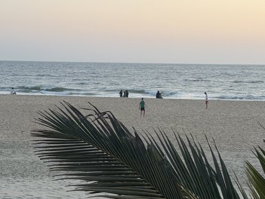 Ein ruhiger Strand mit sanften Wellen, während Menschen in der Ferne am Wasser spielen und die Abendstimmung genießen.