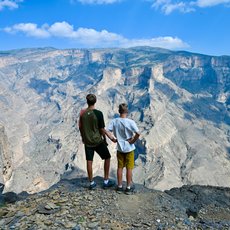 Teenager und Kind blicken gemeinsam auf die atemberaubende Schluchtlandschaft des Jebel Shams – Oman mit Kindern