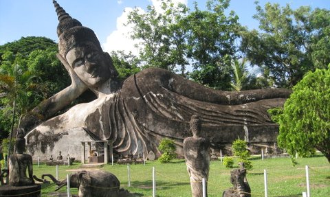 Eine massive, liegende Buddha-Statue dominiert den Park, umgeben von üppigem Grün und weiteren kleineren Statuen.