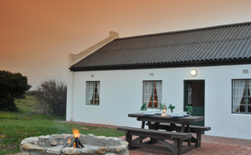 Ein gemütliches Haus mit einem einladenden Außenbereich, umgeben von sanften Hügeln und einem warmen, orangefarbenen Himmel.