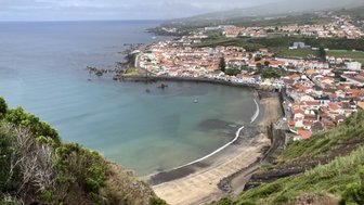 Ein Blick auf die Küste mit bunten Häusern, die sich entlang des Wassers erstrecken, umgeben von sanften Hügeln.