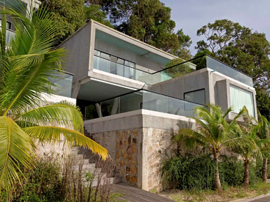 Moderne Villa mit Glasfronten, umgeben von üppigem Grün und Palmen, bietet einen atemberaubenden Blick auf die Natur.