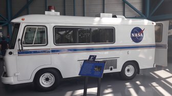 Ein weißer NASA-Astronautenbus steht in einem modernen Ausstellungsraum, umgeben von blauen Stahlträgern.