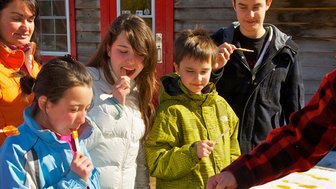 Eine Gruppe von Kindern und Erwachsenen genießt fröhlich eine süße Leckerei im Freien, während die Sonne scheint.
