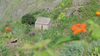 Ein steinernes, traditionelles Haus mit einem strohgedeckten Dach steht malerisch auf einem grünen Hang.