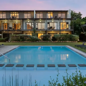 Ein eleganter Pool umgeben von modernen Hotelzimmern, die bei Sonnenuntergang in sanften Farben leuchten.