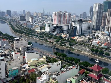 Ein Blick auf die Stadt Saigon mit modernen Hochhäusern und traditionellen Gebäuden entlang eines Flusses unter blauem Himmel.