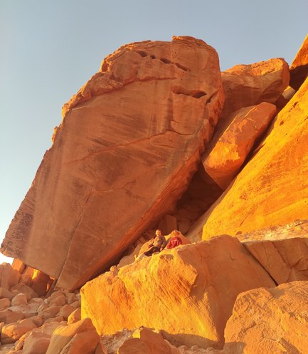 Zwei Personen sitzen auf einem großen Felsen in der Wüste Wadi Rum, umgeben von orangefarbenen Felsformationen.
