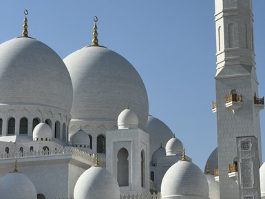 Die beeindruckende Sheikh-Zayed-Moschee in Abu Dhabi mit ihren großen, weißen Kuppeln und dem hohen Minarett unter klarem Himmel.