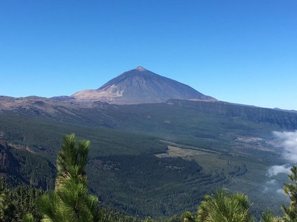 Der majestätische Teide erhebt sich über eine grüne Landschaft, umgeben von klarem, blauem Himmel und sanften Wolken.