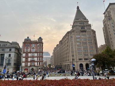 Eine belebte Straße in Shanghai, umgeben von historischen Gebäuden und einer großen Menschenmenge, die sich versammelt.