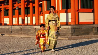 Eine Frau in einem eleganten Kimono und ein kleines Mädchen in einem bunten Kimono spazieren fröhlich im Heian-Schrein.