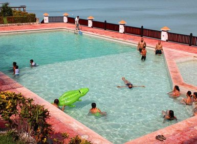 Eine Gruppe von Menschen genießt einen sonnigen Tag am Pool, während Kinder mit einem grünen Krokodil-Schwimmring spielen.