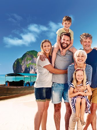 Eine fröhliche Familie posiert am Strand, umgeben von beeindruckenden Klippen und einem Boot im Hintergrund.