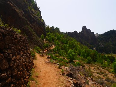 Ein schmaler Weg schlängelt sich durch eine grüne Landschaft, umgeben von hohen Felsen und steilen Hängen.