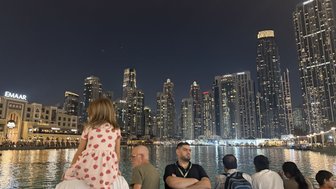 Eine kleine Tochter sitzt auf den Schultern ihres Vaters, während sie die beeindruckende Skyline von Dubai bei Nacht bewundern.