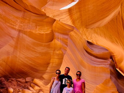 Eine Familie steht in der beeindruckenden Antelope Canyon, umgeben von orangefarbenen Sandsteinformationen und weichem Licht.