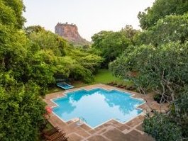 Ein glitzernder Pool umgeben von üppigem Grün, mit dem majestätischen Sigiriya-Felsen im Hintergrund.