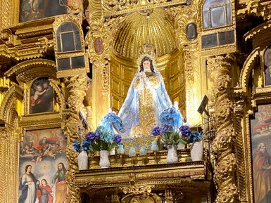 Ein prächtiger Altar mit einer Statue der Jungfrau Maria, umgeben von bunten Blumen und religiösen Bildern im Hintergrund.
