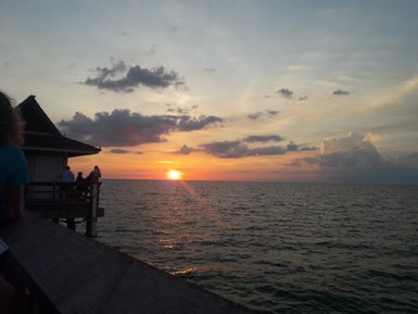 Ein atemberaubender Sonnenuntergang über dem Meer, während Menschen auf einem Pier die Aussicht genießen.