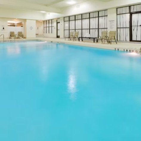 Ein hellblauer Innenpool mit Liegen am Rand, umgeben von großen Fenstern, die natürliches Licht hereinlassen.