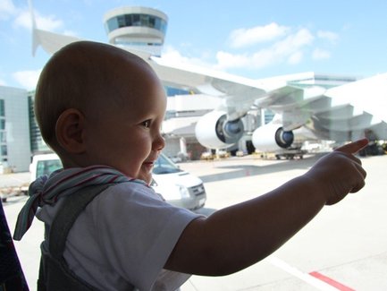 Ein kleines Kind zeigt begeistert auf ein großes Flugzeug, das am Flughafen geparkt ist, während die Sonne scheint.