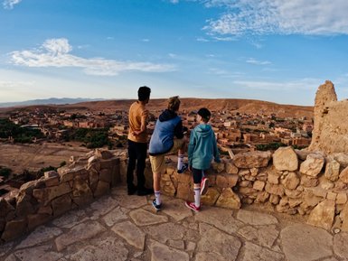 Kinder blicken über eine Mauer auf die Stadt Aït Ben Haddou in Marokko – Familienreise nach Marokko