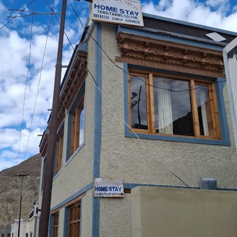 Ein charmantes Homestay in Ladakh mit Holzfenstern und einem einladenden Schild, umgeben von einer malerischen Berglandschaft.