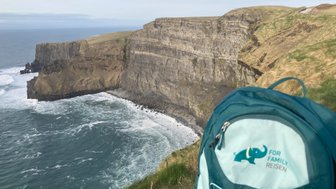 Ein Blick auf die beeindruckenden Cliffs of Moher, mit Wellen, die gegen die Felsen schlagen, und einer grünen Wiese im Vordergrund.