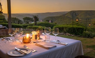 Ein romantisch gedeckter Tisch im Freien, beleuchtet von Kerzen, mit Blick auf die Berge bei Sonnenuntergang.