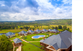 Eine weitläufige Landschaft mit modernen Villen und einem glitzernden Pool, umgeben von sanften Hügeln und bewölktem Himmel.