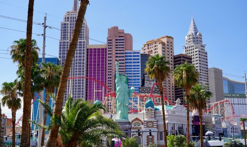 Die Freiheitsstatue steht stolz im Vordergrund, umgeben von Palmen und bunten Wolkenkratzern in Las Vegas.