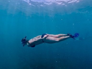 Eine Person taucht elegant unter Wasser und erkundet die ruhigen, blauen Tiefen des Ozeans mit einer Schnorchelausrüstung.