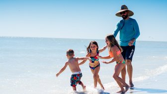Ein Vater spielt mit seinen Kindern am Strand, während sie fröhlich im Wasser planschen und lachen.