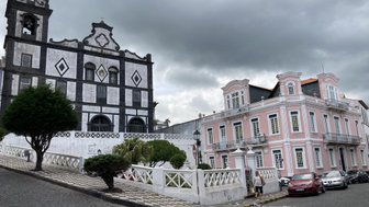 Eine beeindruckende schwarz-weiße Kirche steht neben einem eleganten rosa Gebäude unter einem bewölkten Himmel.