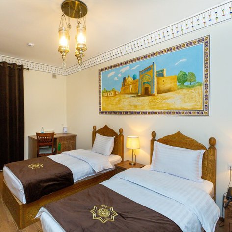 Zwei Einzelbetten mit braunen Bettüberwürfen stehen in einem stilvollen Hotelzimmer mit traditioneller Dekoration.