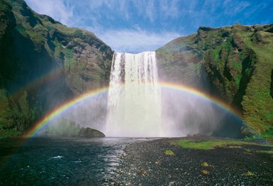 Ein majestätischer Wasserfall stürzt in einen klaren Fluss, während ein strahlender Regenbogen die Szenerie überquert.