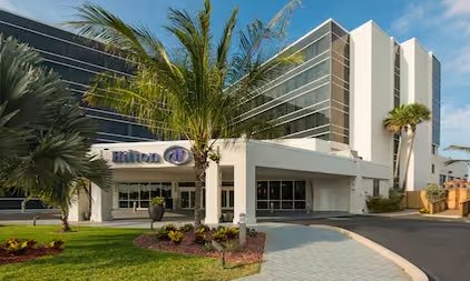 Das Hilton Hotel in Cocoa Beach präsentiert sich mit moderner Architektur und üppiger tropischer Vegetation im Vordergrund.