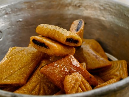 Eine silberne Schüssel voller goldbrauner, süßer Teigstücke, die mit Sirup überzogen sind, vor einem hellen Hintergrund.