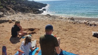 Eine Familie genießt einen sonnigen Tag am Strand, während das Kind im Sand spielt und die Erwachsenen entspannen.